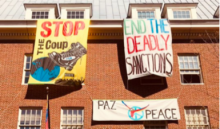 Banners flying on a building reading "Stop the coup," and "End deadly sanctions."